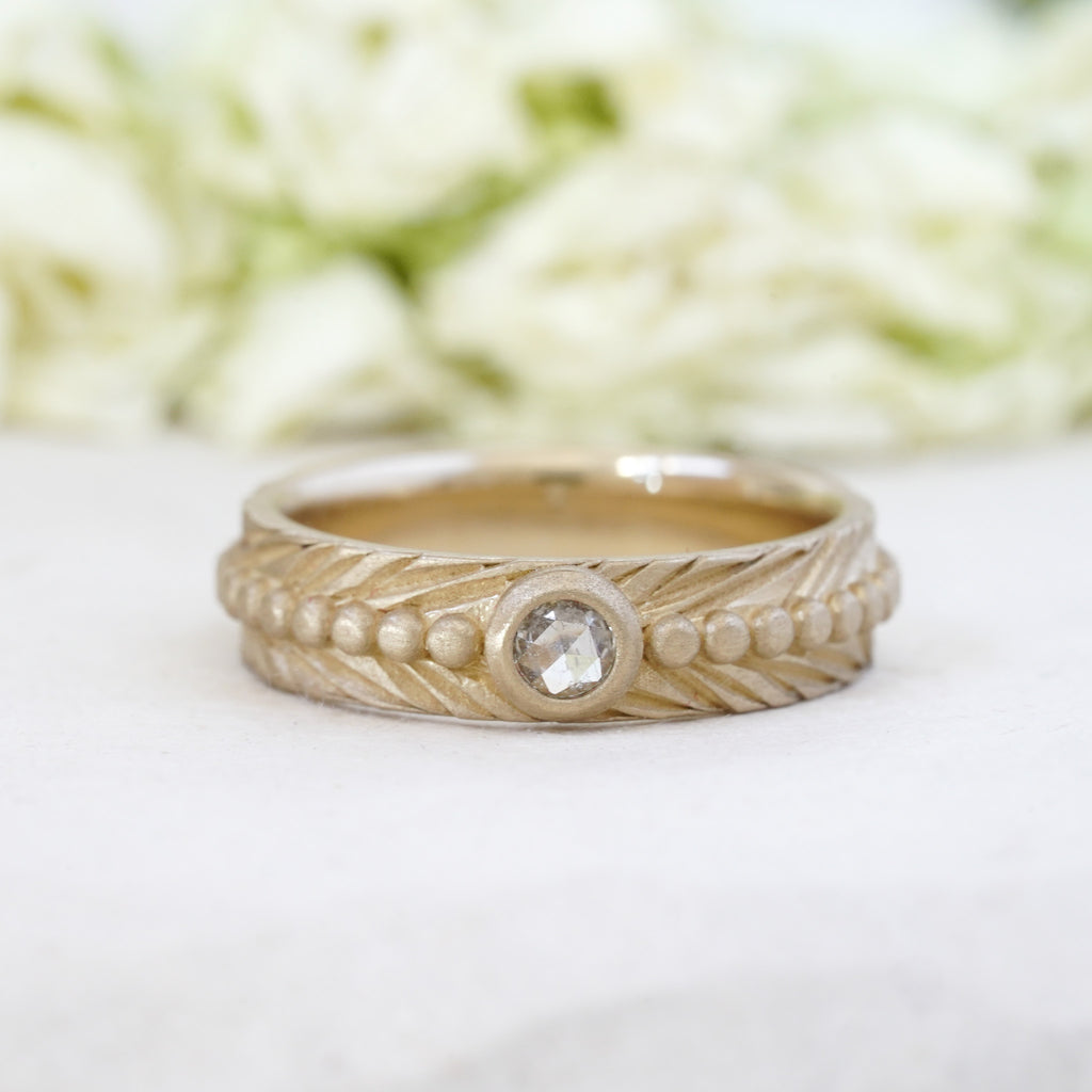 white rosecut diamond bezel set in 14k yellow gold on a engraved feather boho wedding band