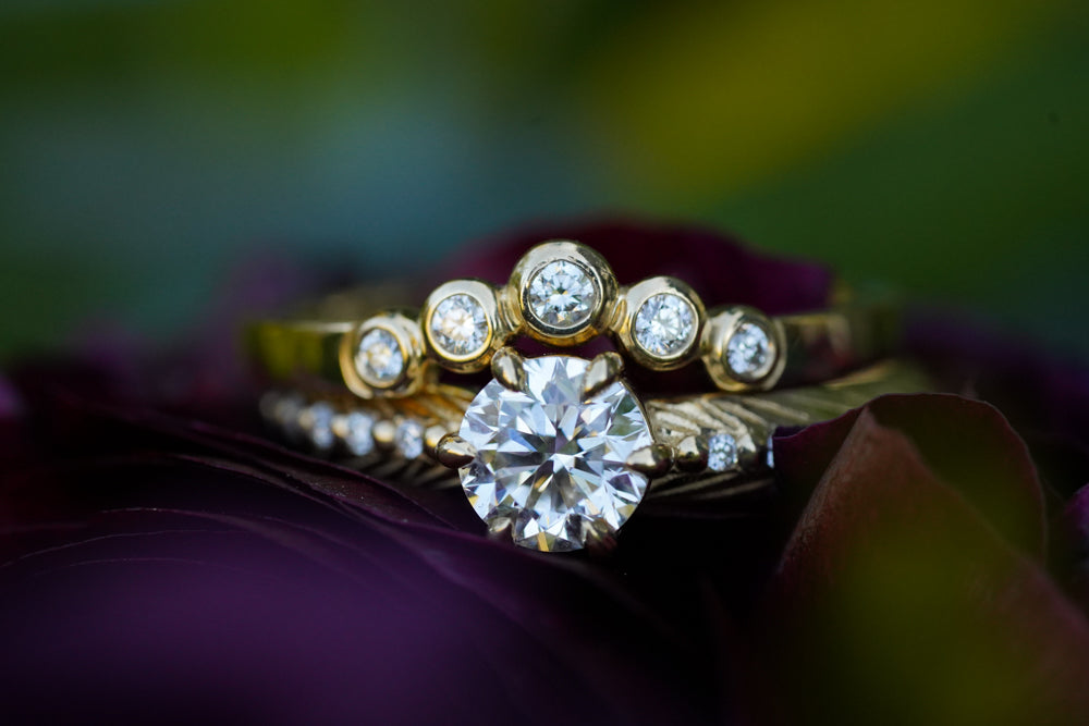 bezel set graduated diamond contour band stacked on top of a prong set round brilliant feather boho engagement ring